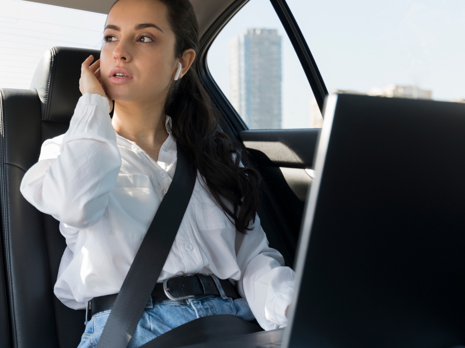 A passenger in the back seat of a car with her laptop open, city towers outside the window.